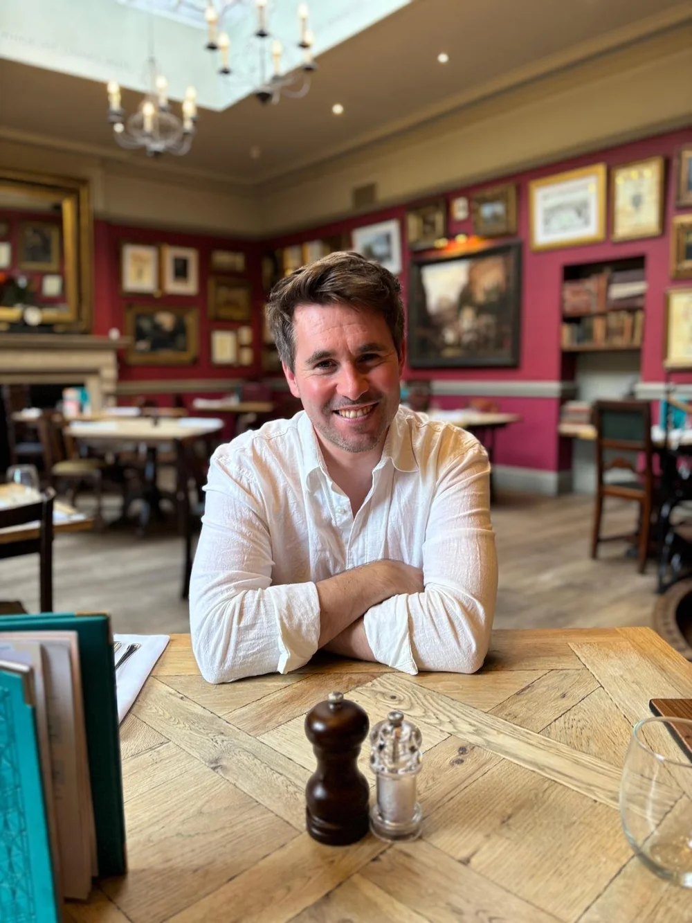 Ben Wooler, smiling, sitting at a wooden table in a restaurant.